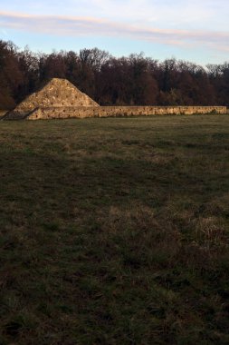 Günbatımında İtalya kırsalında bir ormanın yanındaki çayırda bir manastırın kalıntıları.