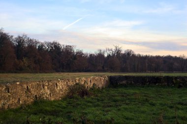 Günbatımında İtalya kırsalında bir ormanın yanındaki çayırda bir manastırın kalıntıları.