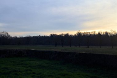 Günbatımında İtalya kırsalında bir ormanın yanındaki çayırda bir manastırın kalıntıları.