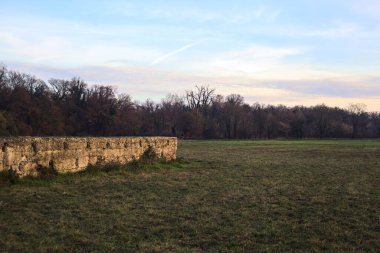 Günbatımında İtalya kırsalında bir ormanın yanındaki çayırda bir manastırın kalıntıları.