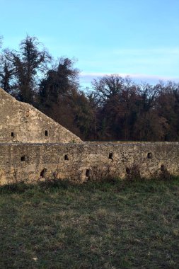 Günbatımında İtalya kırsalında bir ormanın yanındaki çayırda bir manastırın kalıntıları.