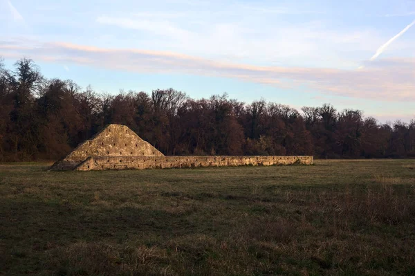 Günbatımında İtalya kırsalında bir ormanın yanındaki çayırda bir manastırın kalıntıları.