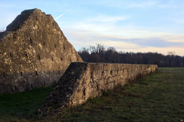 Günbatımında İtalya kırsalında bir ormanın yanındaki çayırda bir manastırın kalıntıları.