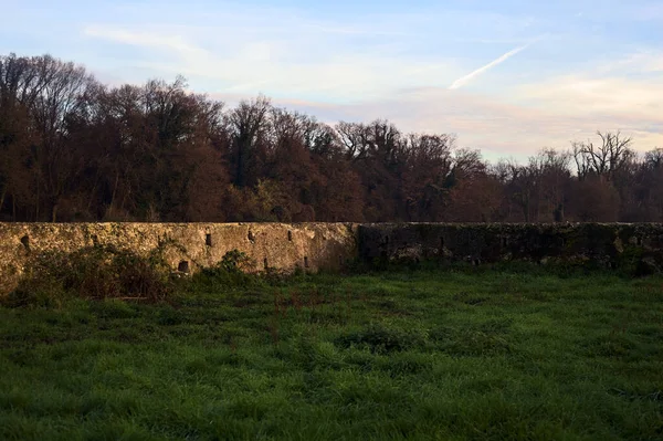 Günbatımında İtalya kırsalında bir ormanın yanındaki çayırda bir manastırın kalıntıları.