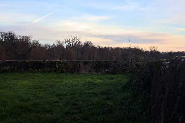 Günbatımında İtalya kırsalında bir ormanın yanındaki çayırda bir manastırın kalıntıları.