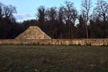 Günbatımında İtalya kırsalında bir ormanın yanındaki çayırda bir manastırın kalıntıları.