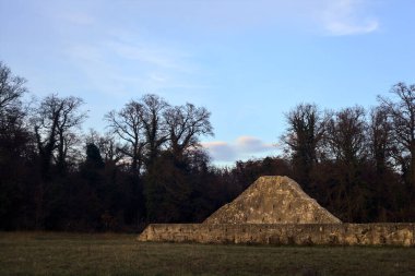 Günbatımında İtalya kırsalında bir ormanın yanındaki çayırda bir manastırın kalıntıları.