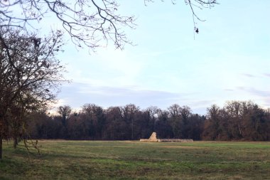 Günbatımında İtalya kırsalında bir ormanın yanındaki çayırda bir manastırın kalıntıları.