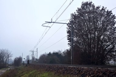 Railroad track on the top of an embankment with bare trees on a misty day in the italian countryside