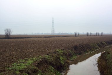 Stream of water between cultivated fields seen from a bridge on a cloudy day in the italian countryside in winter