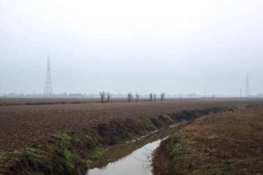 Stream of water between cultivated fields seen from a bridge on a cloudy day in the italian countryside in winter