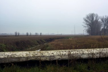 Stream of water between cultivated fields seen from a bridge on a cloudy day in the italian countryside in winter