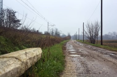 Dirt road and a bridge next to an embankment and a railroad track on a cloudy day in the italian countryside in winter
