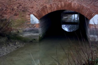 Stream of water between cultivated fields seen from a bridge on a cloudy day in the italian countryside in winter