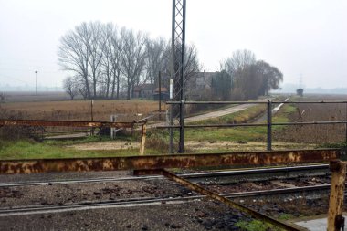 Railroad crossing with rusty bars blocking it on a cloudy day in the italian countryside in winter