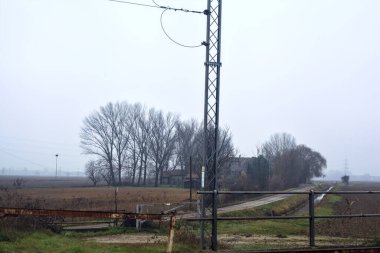 Railroad crossing with rusty bars blocking it on a cloudy day in the italian countryside in winter