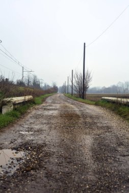 Dirt road and a bridge next to an embankment and a railroad track on a cloudy day in the italian countryside in winter