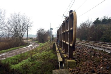 Dirt road and a bridge next to an embankment and a railroad track on a cloudy day in the italian countryside in winter