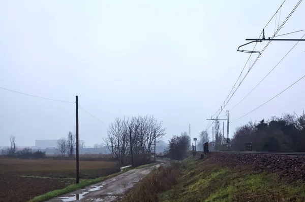Dirt road and a bridge next to an embankment and a railroad track on a cloudy day in the italian countryside in winter