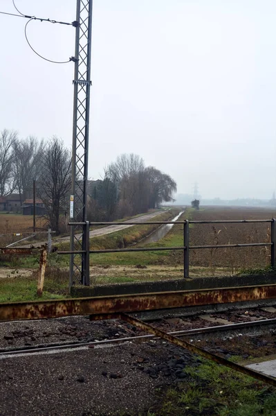 Railroad crossing with rusty bars blocking it on a cloudy day in the italian countryside in winter
