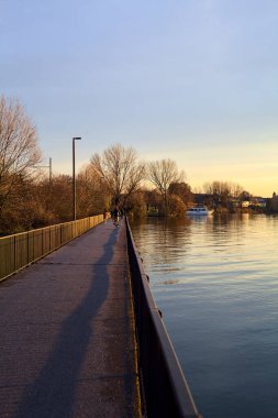 Paved footbridge in a park over a lake at sunset
