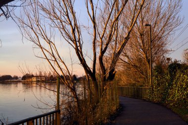 Paved footbridge in a park over a lake at sunset