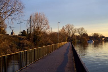Paved footbridge in a park over a lake at sunset