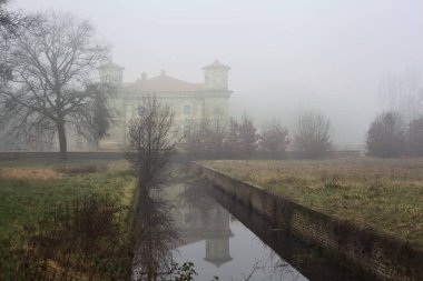 Moat next to a palace in a park on a foggy day in the italian countryside