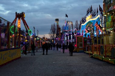 Rides in a fair at dusk with people passing by