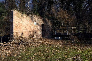 Remains of a facade with an opening on a field next to a stream of water in a park in the italian countryside