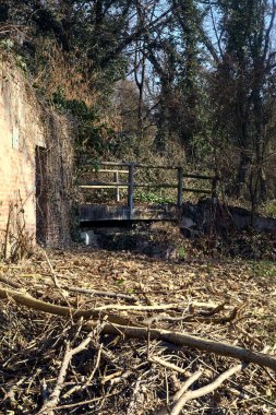 Remains of a facade with an opening on a field next to a stream of water in a park in the italian countryside