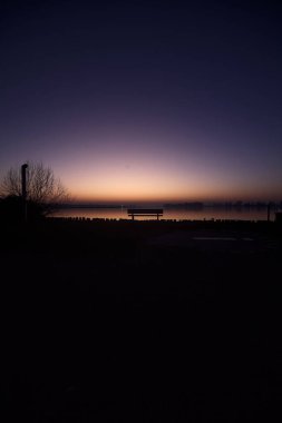 Bench next to the lakeshore at sunset with sky casted in the water