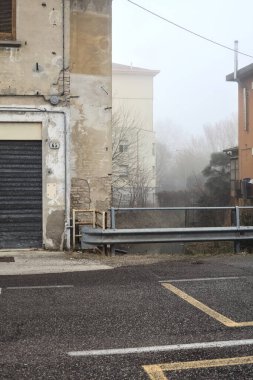 Stream of water between buildings seen from a road on a foggy day in winter