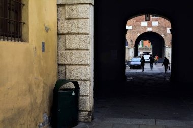 Bir İtalyan şehrinin meydanının gölgesinde, insanların geçtiği kapalı bir sokak.