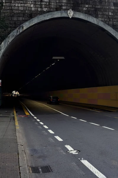 Tunnel under a cliff in an italian city with people and cars passing by