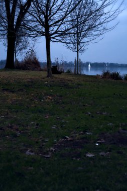 Gün batımında göl ve bulutlu bir günde kıyıdan görünen bir yelkenli.