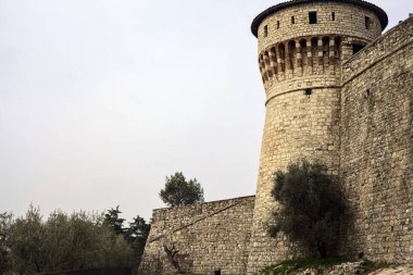 Bulutlu bir günde, bir kulenin yanında çakıl yolu ve yanında zeytin ağacı olan bir sınır duvarı.