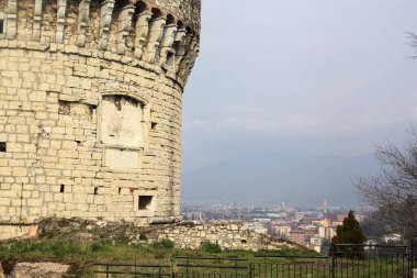 Bulutlu bir günde bir şatonun kulesi tarafından çerçevelenmiş bir parktan görünen şehir.