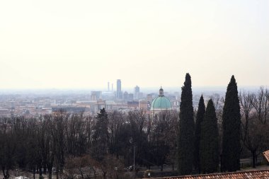 Ufuk çizgisine kadar uzanan şehir bulutlu bir günde ağaçlar ve çatılar tarafından çerçevelenmiş.