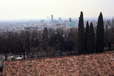 Ufuk çizgisine kadar uzanan şehir bulutlu bir günde ağaçlar ve çatılar tarafından çerçevelenmiş.