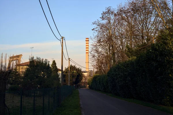 Road in a village in the countryside at sunset with a smokestack in the distance