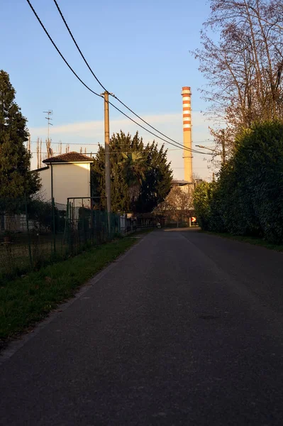 Road in a village in the countryside at sunset with a smokestack in the distance