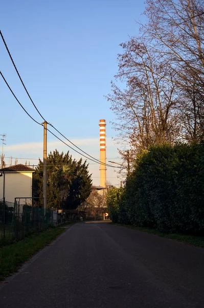 stock image Road in a village in the countryside at sunset with a smokestack in the distance