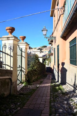 Güneşli bir günde, deniz kenarında bir tepede patika bir sokak.