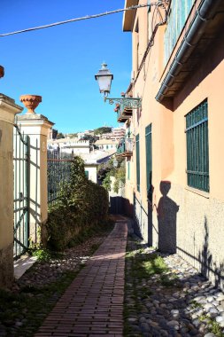 Güneşli bir günde, deniz kenarında bir tepede patika bir sokak.