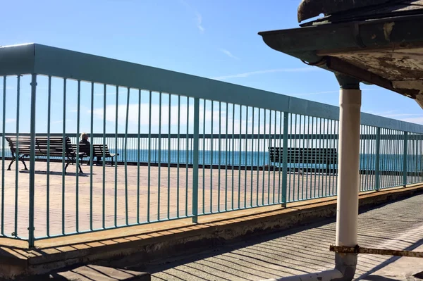 Woman sittng on a bench on a panoramic terrace by the sea on a sunny day seen through a railing
