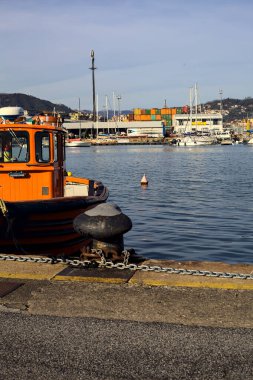 Gün batımında arkaplanda yük deposu olan bir iskelede turuncu tekne.