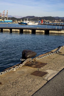 Gün batımında bir körfezde, uzak mesafeden görülen bir nakliye deposu ve bir sanayi tesisi.