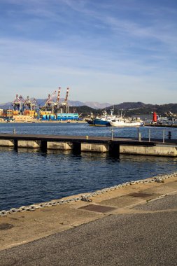 Gün batımında bir körfezde, uzak mesafeden görülen bir nakliye deposu ve bir sanayi tesisi.