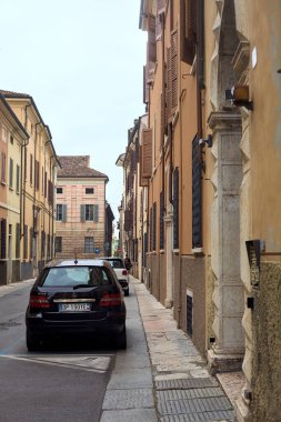 Bulutlu bir günde dar bir caddede, park halindeki arabaların olduğu bir yerde.